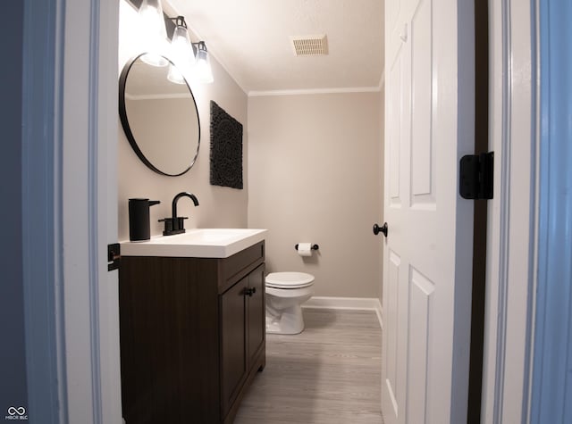 half bathroom featuring visible vents, toilet, ornamental molding, vanity, and wood finished floors