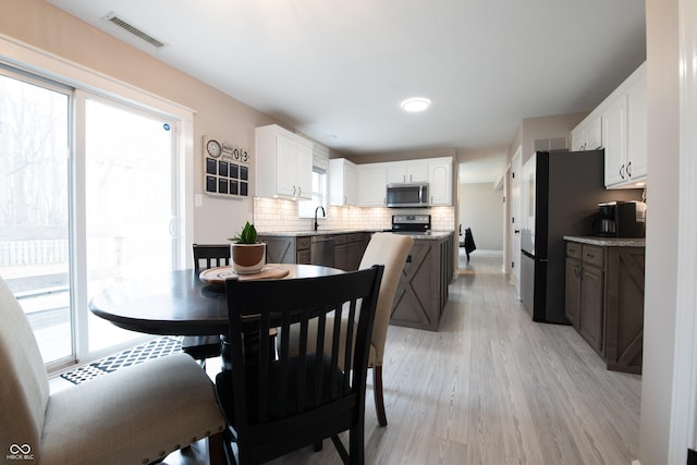 dining area with light wood-type flooring, visible vents, and baseboards