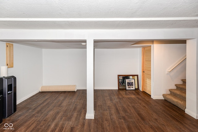 finished below grade area with a textured ceiling, dark wood-type flooring, stairway, and baseboards