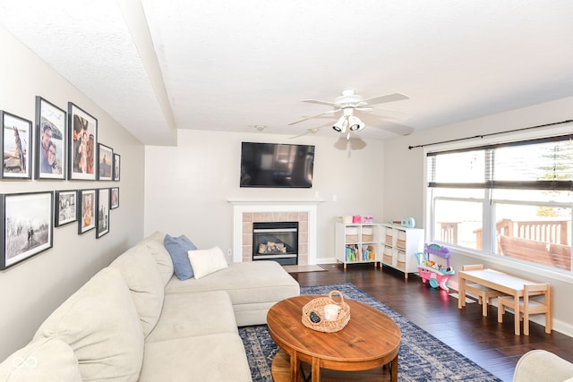 living room with ceiling fan, a tiled fireplace, wood finished floors, and baseboards