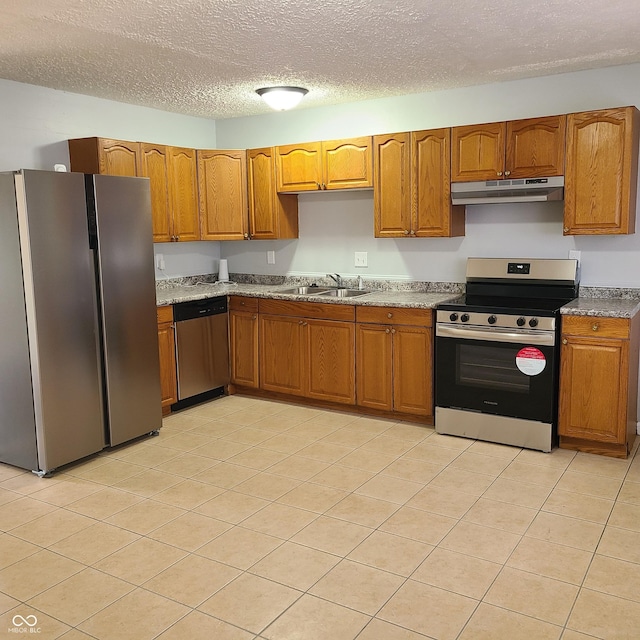 kitchen with appliances with stainless steel finishes, brown cabinetry, a sink, and under cabinet range hood