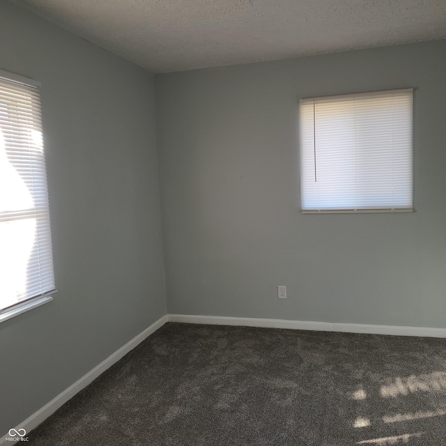 spare room with dark colored carpet, a textured ceiling, and baseboards