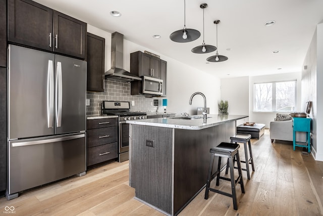 kitchen with a sink, appliances with stainless steel finishes, light wood-type flooring, and wall chimney range hood