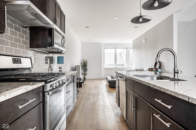 kitchen featuring dark brown cabinetry, a sink, wall chimney range hood, appliances with stainless steel finishes, and backsplash