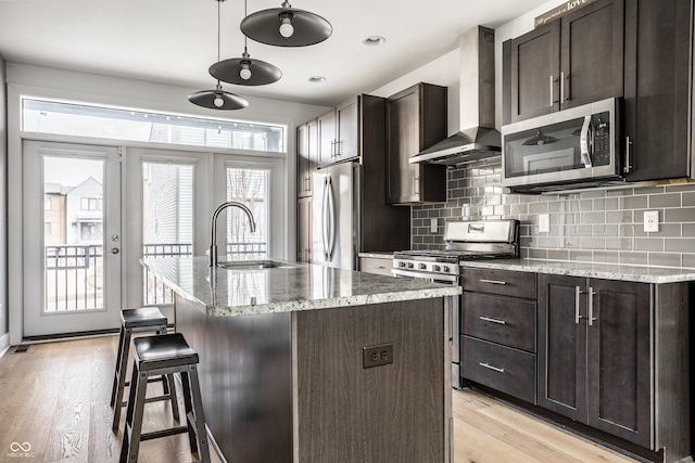 kitchen featuring stainless steel appliances, a sink, light wood finished floors, and wall chimney exhaust hood