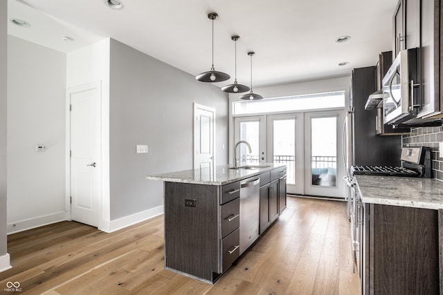 kitchen with dark brown cabinets, appliances with stainless steel finishes, light wood-type flooring, and backsplash