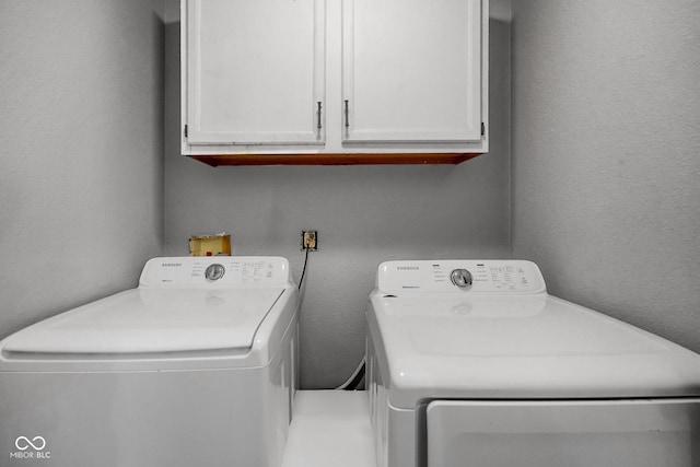 clothes washing area with a textured wall, washing machine and clothes dryer, and cabinet space