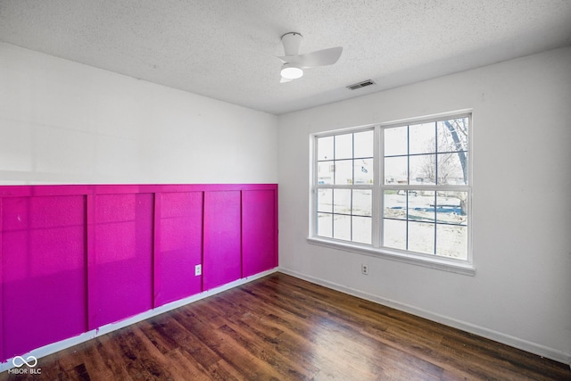 spare room with a textured ceiling, wood finished floors, visible vents, and baseboards