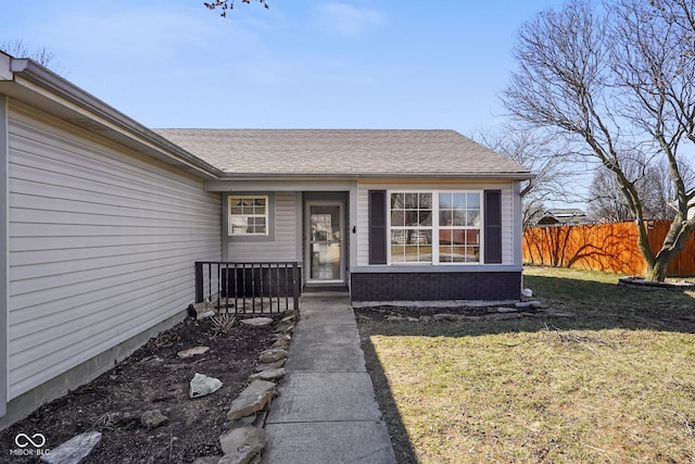 entrance to property with a shingled roof, fence, and a yard