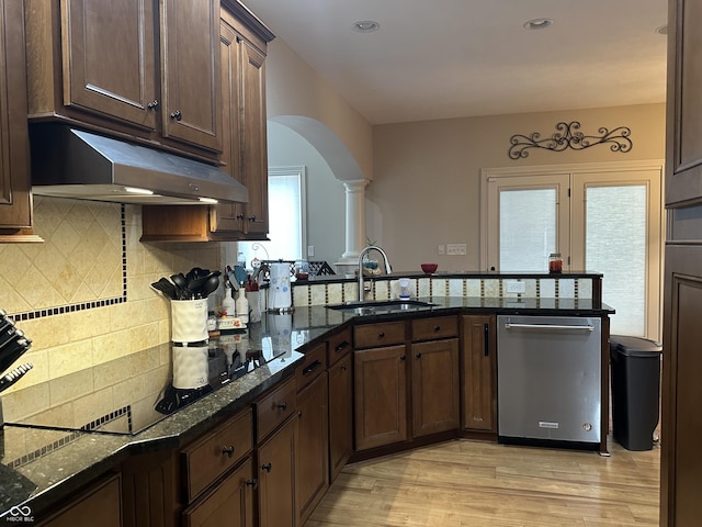 kitchen with arched walkways, light wood-style flooring, stainless steel dishwasher, a sink, and under cabinet range hood