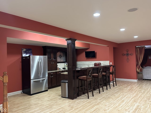 kitchen with freestanding refrigerator, baseboards, light wood finished floors, and a kitchen bar