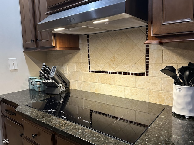 kitchen with backsplash, dark stone countertops, dark brown cabinets, under cabinet range hood, and black electric cooktop