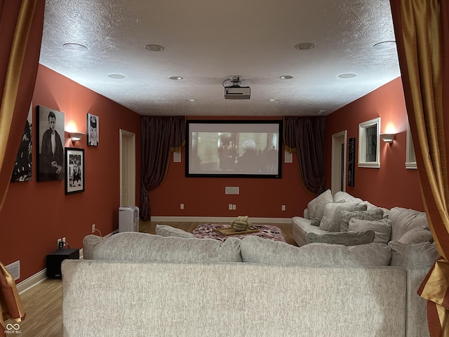 home theater room with light wood-type flooring, baseboards, visible vents, and a textured ceiling