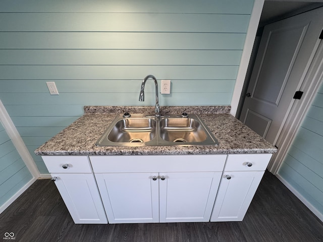 kitchen featuring dark wood-style floors, white cabinetry, a sink, wooden walls, and baseboards