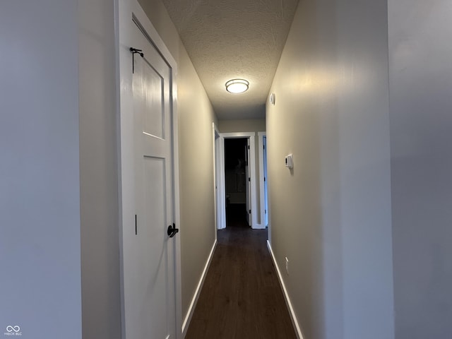 hall with a textured ceiling, dark wood finished floors, and baseboards