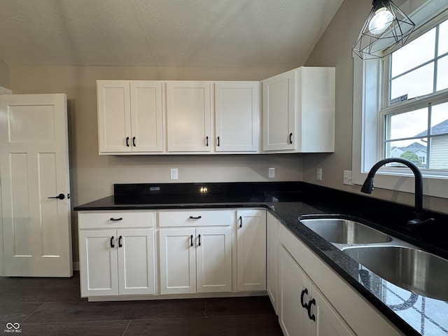 kitchen with dark wood-style floors, white cabinets, a sink, a textured ceiling, and dark stone counters