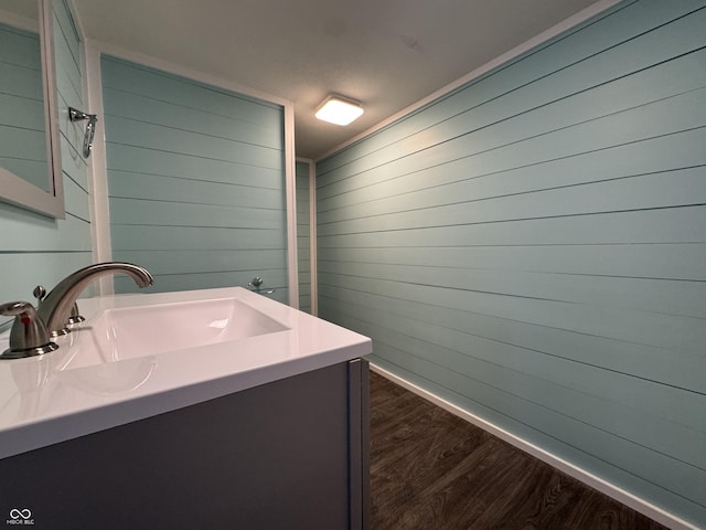 bathroom featuring wooden walls, baseboards, wood finished floors, and vanity