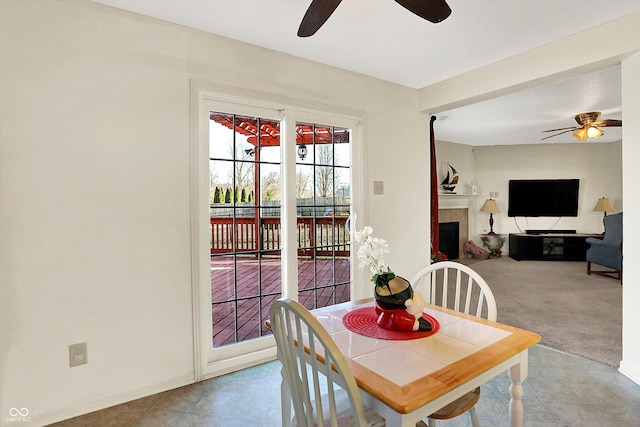 dining room with carpet floors, a ceiling fan, and a tiled fireplace