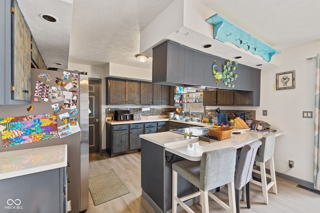 kitchen featuring light wood-style flooring, light countertops, freestanding refrigerator, tasteful backsplash, and a kitchen bar