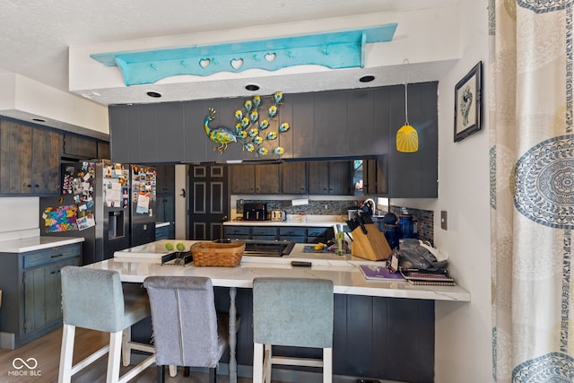 kitchen with light countertops, dark brown cabinetry, stainless steel refrigerator with ice dispenser, and a peninsula