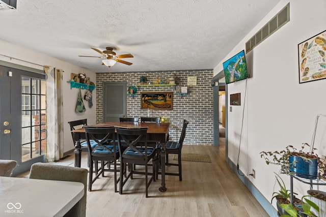 dining space with visible vents, a ceiling fan, a textured ceiling, brick wall, and wood finished floors