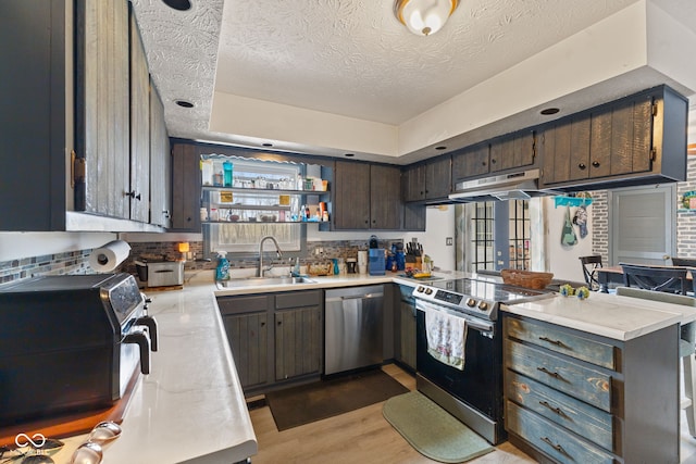 kitchen featuring stainless steel appliances, light countertops, a sink, a peninsula, and under cabinet range hood