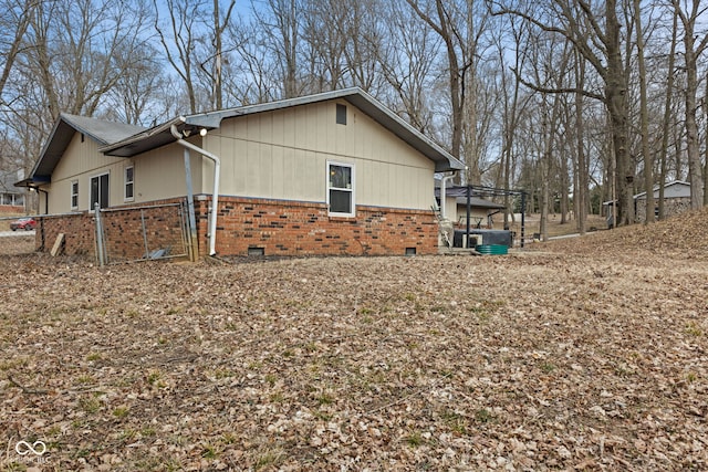 view of side of property featuring crawl space, brick siding, fence, and central AC unit