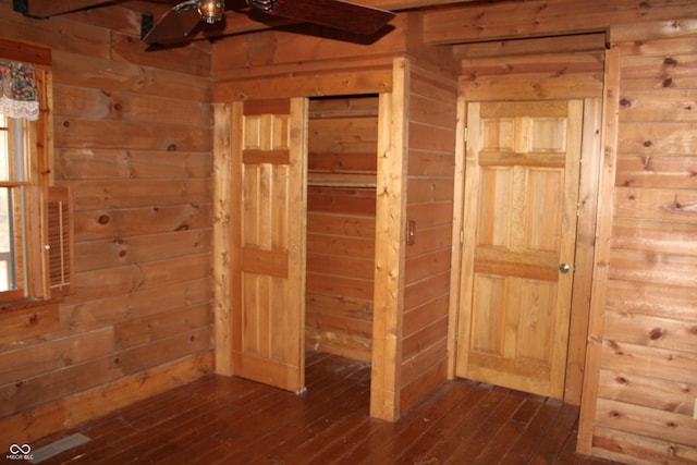 unfurnished room with dark wood-type flooring, wood walls, and a ceiling fan