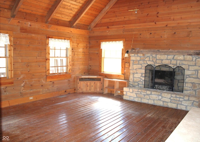 unfurnished living room with vaulted ceiling with beams, a stone fireplace, wood walls, and hardwood / wood-style floors