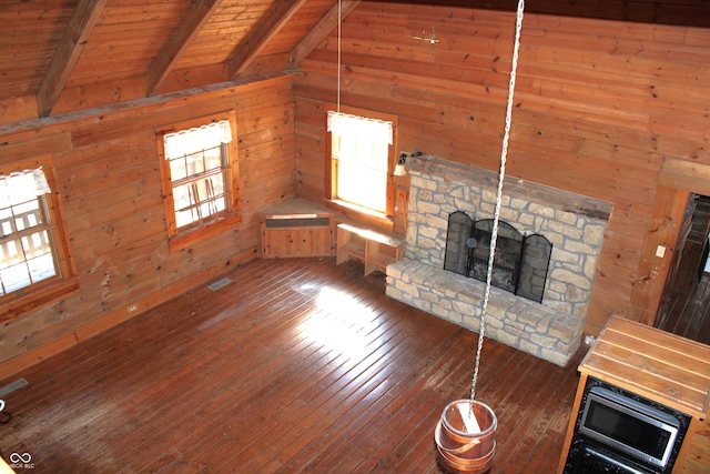 unfurnished living room featuring lofted ceiling with beams, a stone fireplace, wooden ceiling, hardwood / wood-style flooring, and wooden walls