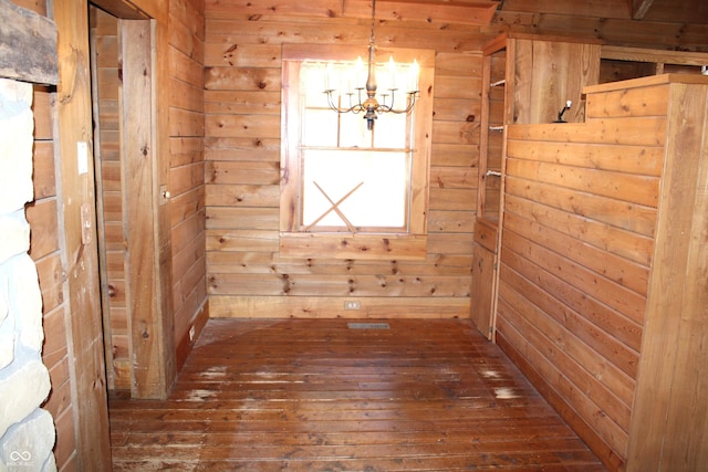 empty room featuring a chandelier, wood walls, and dark wood finished floors