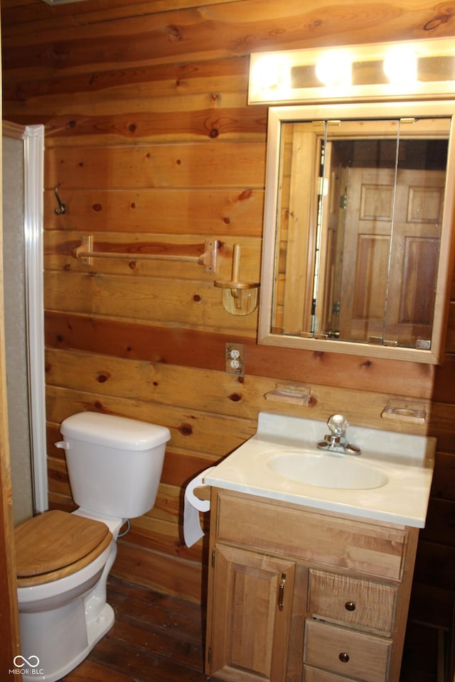 half bathroom featuring wood finished floors, wood walls, vanity, and toilet