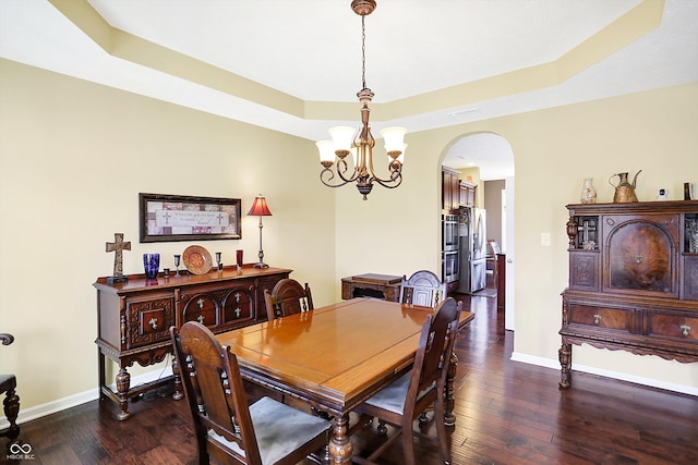 dining area with arched walkways, a tray ceiling, dark wood-type flooring, a chandelier, and baseboards