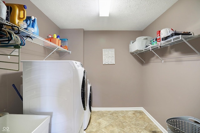 washroom with a textured ceiling, laundry area, separate washer and dryer, a sink, and baseboards