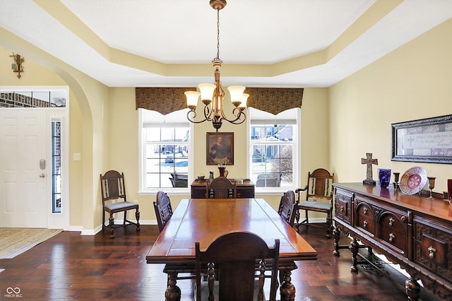 dining area featuring arched walkways, a raised ceiling, an inviting chandelier, wood finished floors, and baseboards