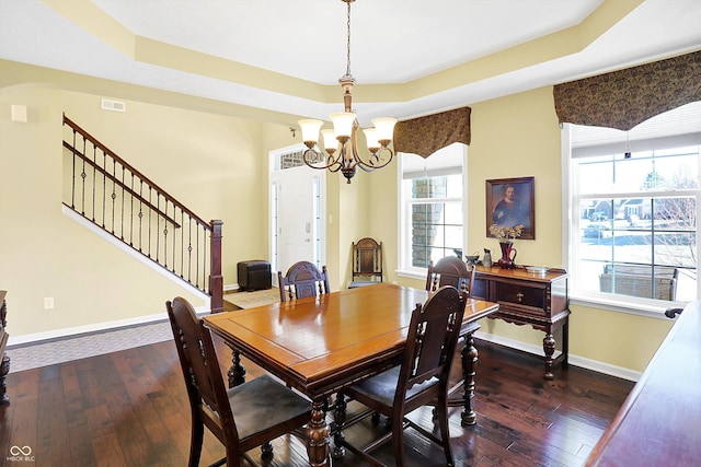 dining area with a healthy amount of sunlight, dark wood-style floors, stairs, and a tray ceiling