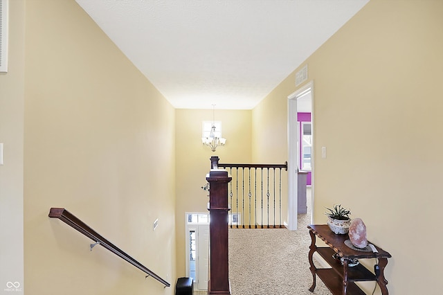 hallway with a chandelier, carpet flooring, visible vents, a healthy amount of sunlight, and an upstairs landing