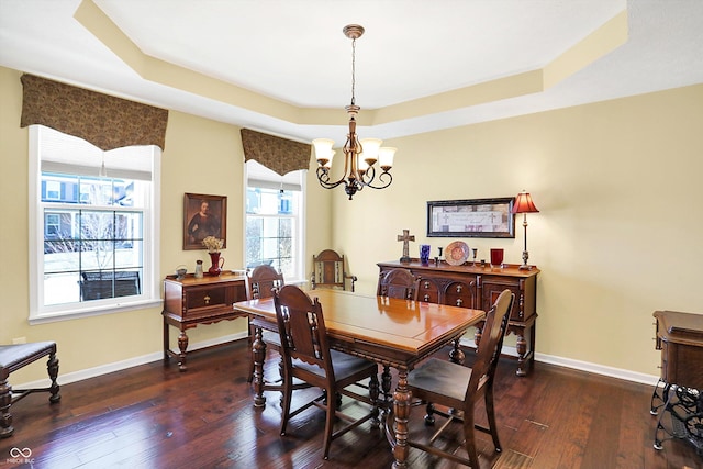 dining area with baseboards, a tray ceiling, dark wood finished floors, and a notable chandelier