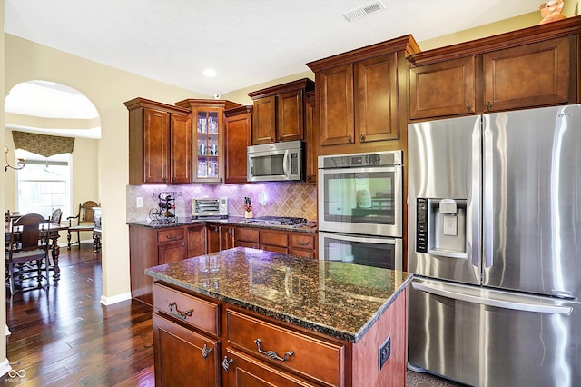 kitchen with stainless steel appliances, visible vents, glass insert cabinets, and backsplash