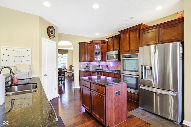 kitchen featuring arched walkways, a sink, appliances with stainless steel finishes, tasteful backsplash, and dark stone countertops