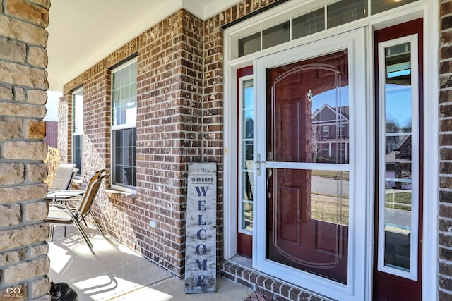 entrance to property featuring a porch and brick siding