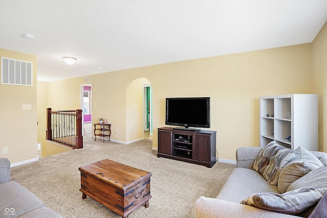 living room featuring arched walkways, baseboards, visible vents, and light colored carpet