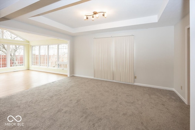 carpeted empty room with a raised ceiling and baseboards