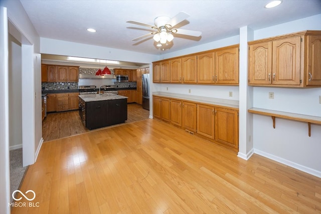 kitchen featuring light wood finished floors, appliances with stainless steel finishes, a center island with sink, and brown cabinets