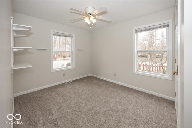 carpeted empty room with baseboards, visible vents, and a ceiling fan