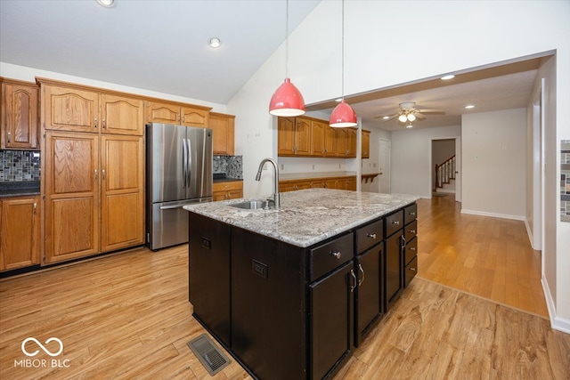 kitchen with pendant lighting, visible vents, light wood-style floors, freestanding refrigerator, and a sink