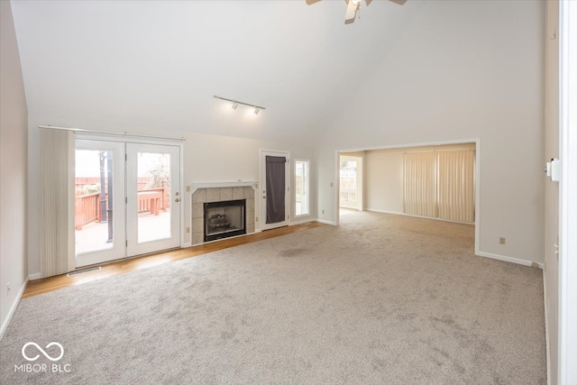 unfurnished living room with baseboards, rail lighting, carpet floors, a fireplace, and high vaulted ceiling