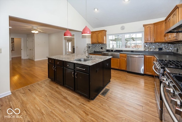 kitchen featuring stainless steel appliances, a sink, light wood finished floors, and an island with sink