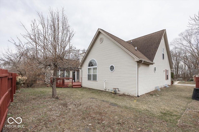 view of property exterior featuring roof with shingles, fence, a lawn, and a wooden deck