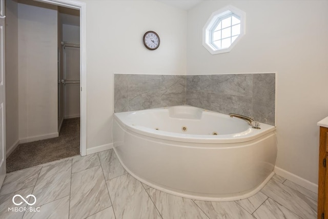 bathroom featuring a jetted tub, marble finish floor, baseboards, and vanity